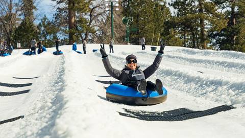 An adult in a snow tube flying down a lane at Snow Valley's Coyote Creek Tube Park