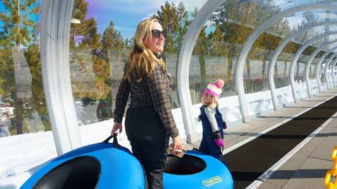 An adult and child holding snow tube on the Snow Valley Coyote Creek Tube Park lift conveyor that escorts guests to the top of the tubing hill